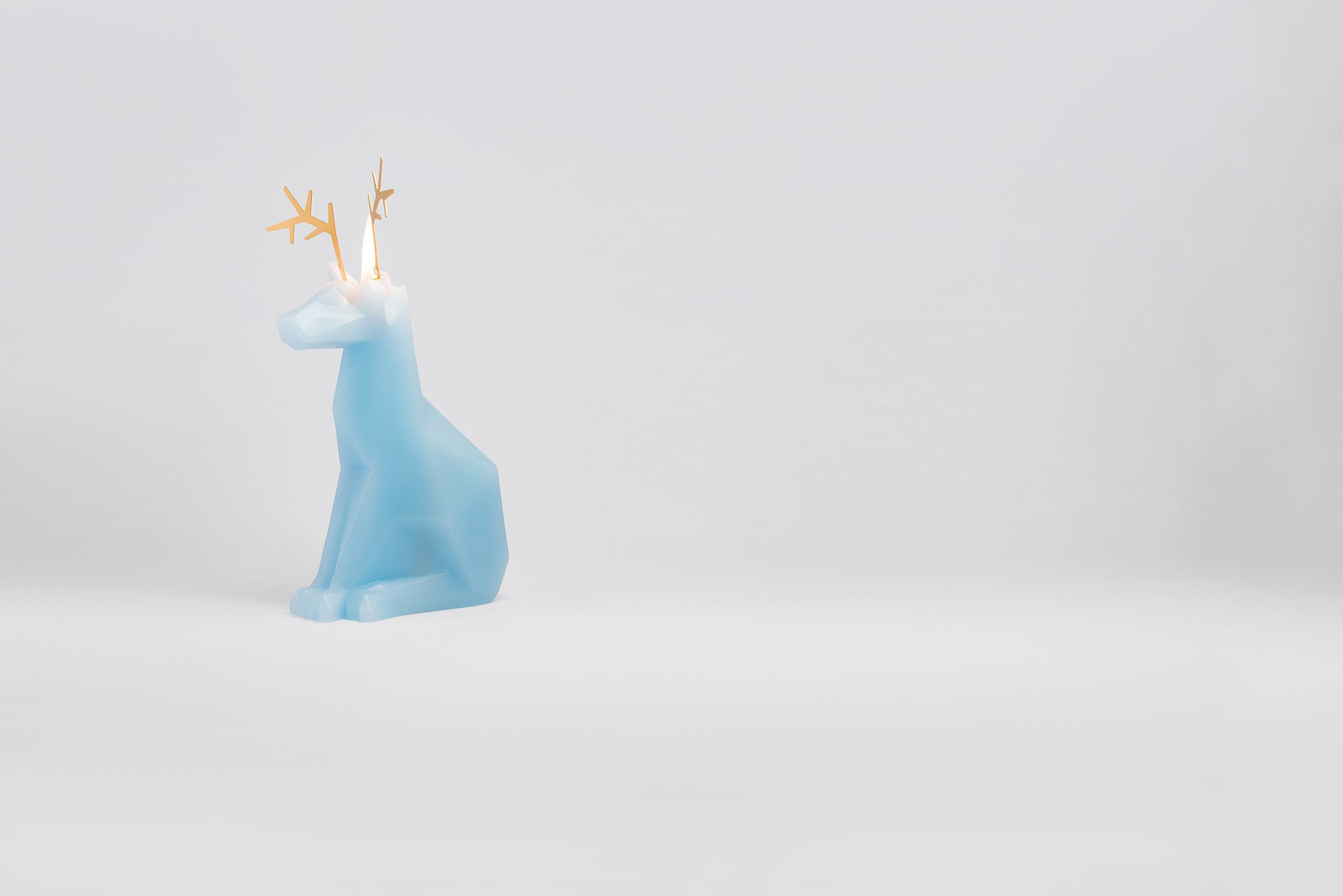 Side view of light blue dyri the reindeer pyropet candle with a lit wick. 