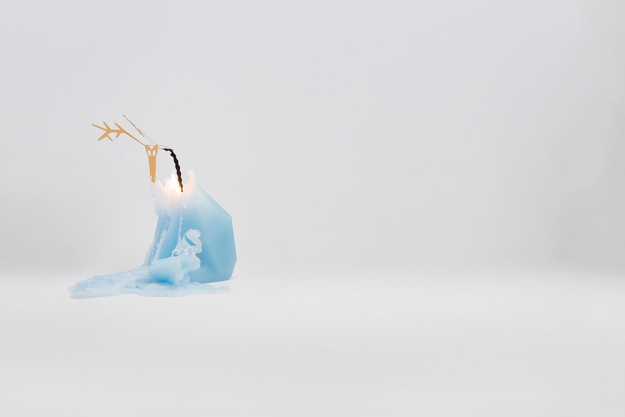 Side view of burning, light blue dyri the reindeer pyropet candle. As the wax melts the inner skeleton frame is revealed. 