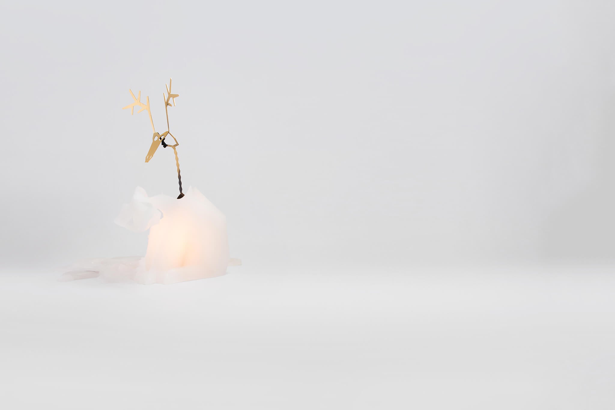 Side view of white dyri reindeer pyropet candle. It has been lit and is melted halfway revealing the inner skeleton suprise. 