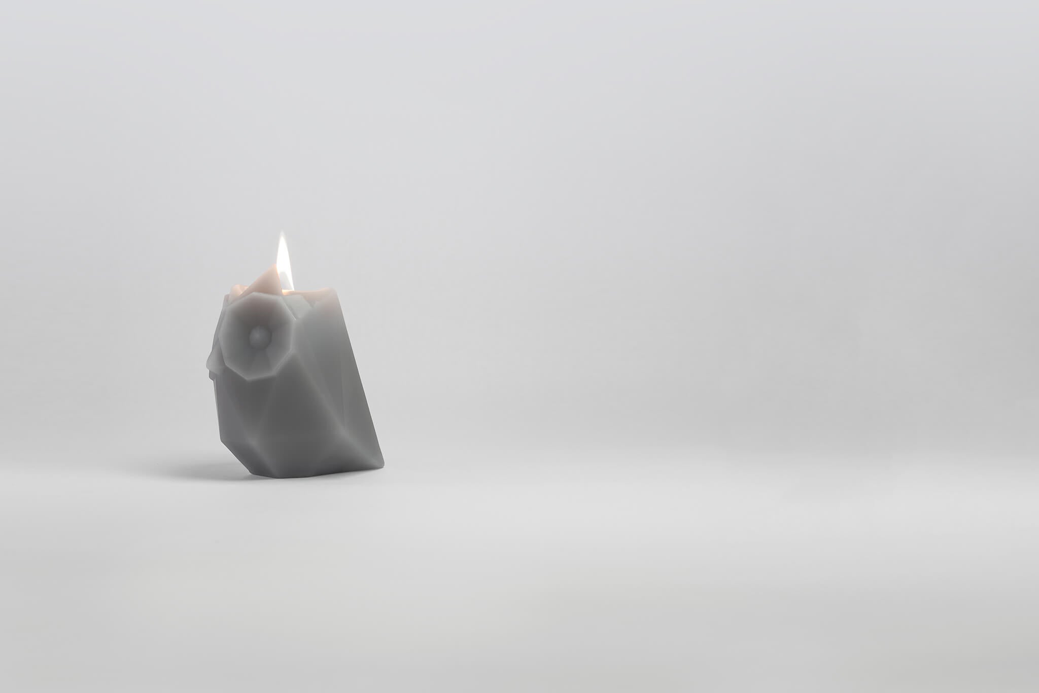 Side view of Ugla, the grey owl-shaped pyropet candle with a burning wick. 